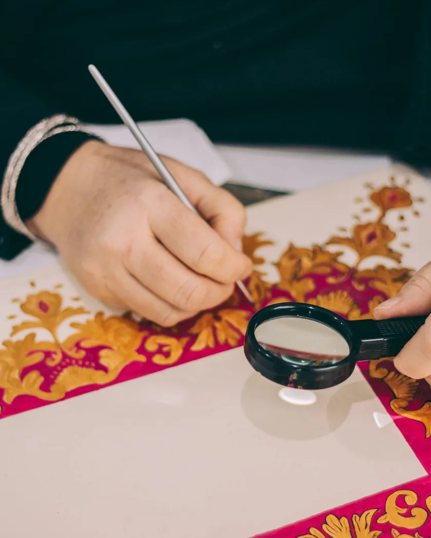 Detalle de manos trabajando motivos dorados sobre una pieza decorativa pintada a mano